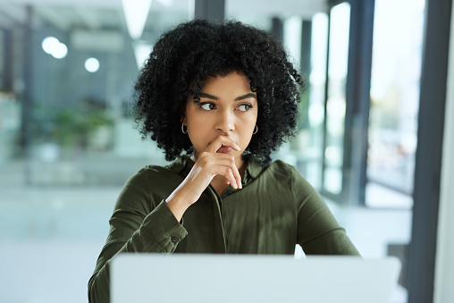 Shot of a young businesswoman looking thoughtful while using a laptop in a modern office